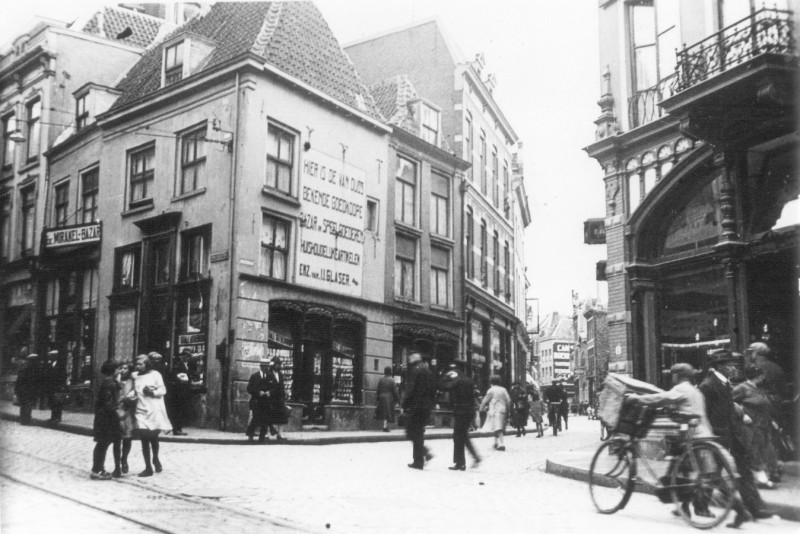 Het hoekpand is de winkel van Helena Egger. De ‘Mirakelbazar’ heeft twee ingangen en loopt achter Helena’s pand door. Wanneer de foto genomen wordt in 1926, staat deze bazaar op het punt om naar de overkant te verhuizen, zoals ook het bord aangeeft. Ook op het bord boven de ingang aan de Stikke Hezelstraat, de straat links, staat ‘Mirakelbazar’. Recht tegenover deze ingang werd enige tijd later de winkel van Voltijn en Ketellapper gevestigd.